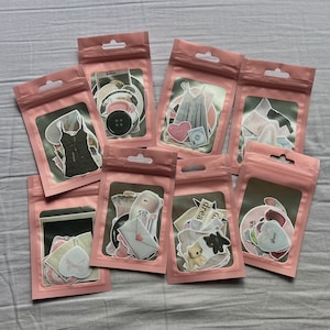 May include: Nine pink zippered pouches with various colorful patterned stickers and illustrations inside. The pouches are arranged in a semi-circle on a white surface.