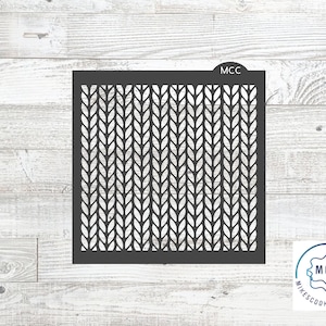 May include: Black stencil with a repeating pattern of knitted stitches. The stencil is labeled "MCC" in the top right corner. The stencil is on a white wood background.
