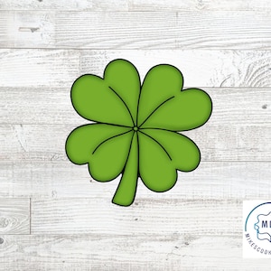 Puede incluir: Cortador de galletas de trébol de cuatro hojas verde. El cortador está hecho de metal y tiene un acabado liso y brillante.