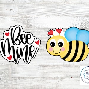 May include: Bee Mine cookie cutter with a bee design. The bee is yellow and black with blue wings and red hearts on its head. The bee mine cookie cutter is white with black lettering and red hearts.