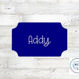 May include: A blue cookie cutter with a scalloped edge and the name "Addy" written in white.