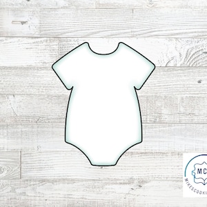 May include: A white outline of a baby onesie on a woodgrain background. The onesie has a short sleeve and a rounded neckline.
