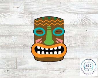 Puede incluir: Un cortador de galletas de máscara tiki marrón con una nariz verde, ojos azules y una amplia sonrisa con dientes. La máscara tiene un diseño marrón, naranja y verde.