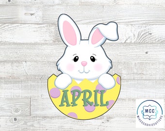 May include: A white bunny peeking out of a yellow and purple Easter egg with the word "APRIL" written in green letters.
