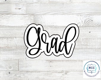 May include: A black cookie cutter in the shape of the word "Grad" in a cursive font. The cutter is on a light wood grain background. A small logo is in the bottom right corner.