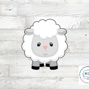 May include: A white sheep cookie cutter with a gray face and pink nose. The cookie cutter is on a white wood background.