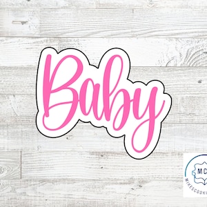 May include: A pink "Baby" cookie cutter with a black outline, set against a light wood grain background. The word "Baby" is written in a cursive font. A logo for Mike's Cookie Cutters is in the bottom right corner.