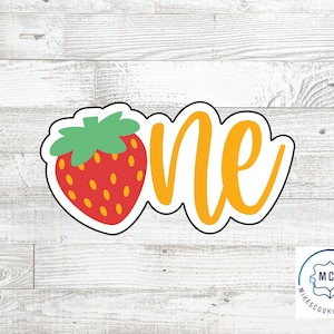 May include: A cookie cutter in the shape of a strawberry with the word "one" in a cursive font. The strawberry is red with yellow seeds and a green stem. The word "one" is yellow.