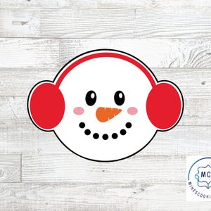Può includere: Un tagliapasta a forma di pupazzo di neve bianco con paraorecchie rosse. Il pupazzo di neve ha un naso di carota, occhi neri e una bocca nera.