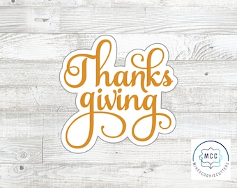 May include: A cookie cutter shaped like the word Thanksgiving in a cursive script font. The cutter has a thick orange outline and a white interior, with the text Thanks and giving stacked vertically in a flowing, connected lettering style.