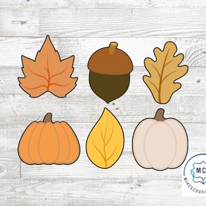 Könnte beinhalten: Satz mit sechs Ausstechern zum Thema Herbst. Die Ausstecher sind in Form eines Ahornblattes, Eichenblattes, einer Eichel, eines Kürbisses und zweier verschiedener Blätter. Die Ausstecher sind aus Metall und haben eine silberne Oberfläche.
