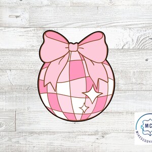 Op de afbeelding: Roze en witte ruitjes kerstbal met een roze strik. De kerstbal heeft een glinsterend ontwerp.