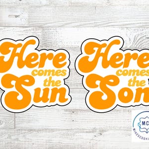 Peut inclure: Deux emportes-pièces en forme des mots "Here comes the Sun" et "Here comes the Son". Les emportes-pièces sont orange et jaune avec un contour blanc.