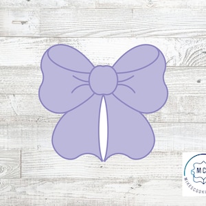 May include: A light purple bow-shaped cookie cutter. The cutter has a detailed design with rounded edges and a central knot. The bow is centered on a light wood grain background. The logo for MikesCookieCutters is in the bottom right corner.