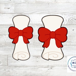 May include: Two white cookie cutters shaped like rolled up diplomas with red bows on top. The cookie cutters are on a white wood background. The text "MCC Mike's Cookie Cutters" is in the lower right corner of the image.
