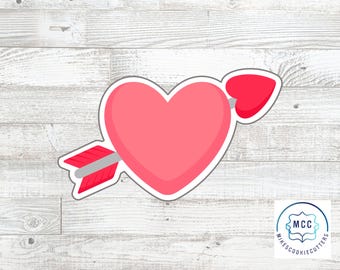 May include: A pink heart pierced by a red arrow, a cookie cutter design. The arrow has a gray shaft and red fletching. The heart and arrow are outlined in white. The logo for MikesCookieCutters is in the bottom right corner.