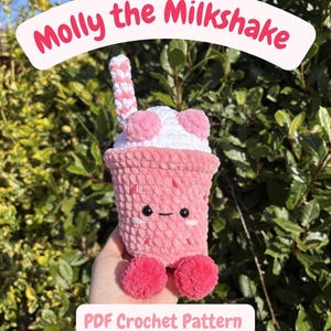 May include: A handmade pink crochet milkshake toy with a white top and pink accents. The toy has a smiling face and two pink pom-pom feet. The text "Molly the Milkshake" and "PDF Crochet Pattern" are displayed.
