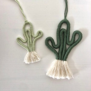Pode incluir: Dois ornamentos de cacto de macramé verde e branco com borlas brancas.