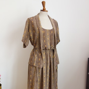 May include: A brown and yellow patterned dress with a matching jacket. The dress has a fitted bodice and a flowing skirt. The jacket has a shawl collar and is open in the front.