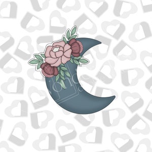 Pode incluir: Cortador de biscoitos em forma de meia-lua em azul-petróleo suave, adornado com um arranjo floral. As flores são rosa claro e bordô, com folhas verdes. O cortador é para assar.