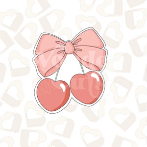 Puede incluir: Dos cerezas rosas con un lazo rosa atado alrededor de sus tallos. Las cerezas están delineadas en negro y tienen un acabado brillante.