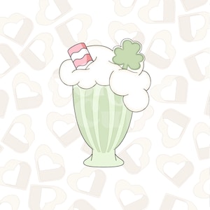 May include: A green milkshake with whipped cream and a red and white striped straw topped with a green shamrock. The background is a pattern of light brown hearts.