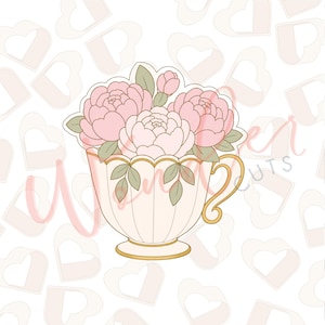 Puede incluir: Cortador de galletas con forma de taza de té llena de peonías rosas y hojas verdes. La taza de té es de color crema con ribetes dorados y un asa decorativa. El fondo es blanco con formas de corazón.