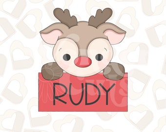 May include: A cute cartoon reindeer with brown antlers and a red nose peeking over a red sign that says "RUDY". The background is a white pattern of hearts.