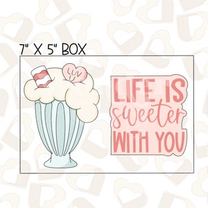 Peut inclure: Une boîte de 18 x 13 cm contenant deux emporte-pièces. Un emporte-pièce est un milk-shake avec un bonbon en forme de cœur sur le dessus. L'autre emporte-pièce est un rectangle rose avec le texte "LIFE IS sweeter WITH YOU".