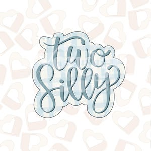 Può includere: Un tagliabiscotti a forma delle parole "Two Silly" in corsivo. Il testo è azzurro chiaro con un motivo a quadri, delineato in blu più scuro. Lo sfondo è bianco con un motivo di cuori rosa chiaro.