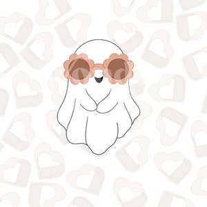 Puede incluir: Un fantasma blanco con gafas de sol de color rosa en forma de flor con lentes marrones. El fantasma sonríe y tiene un cuerpo blanco en forma de sábana. El fondo es un patrón de corazones blancos.