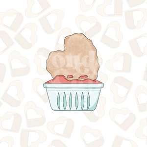 May include: A heart-shaped cookie cutter with a brown, textured surface, sitting in a white and blue plastic basket. The basket has a heart-shaped design.