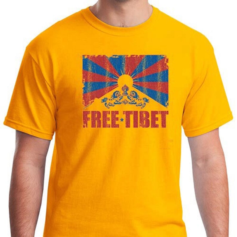 Pu&ograve; includere: Una maglietta gialla con un'immagine usurata della bandiera tibetana e il testo "FREE TIBET" in rosso.