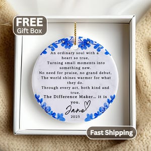 May include: A round white ceramic ornament with a marble texture, featuring a blue floral border and black printed text that reads: An ordinary soul with a heart so true, Turning small moments into something new. No need for praise, no grand debut, The world shines warmer for what they do. Through every act, both kind and true, The Difference Maker... it is you. Jane 2025.