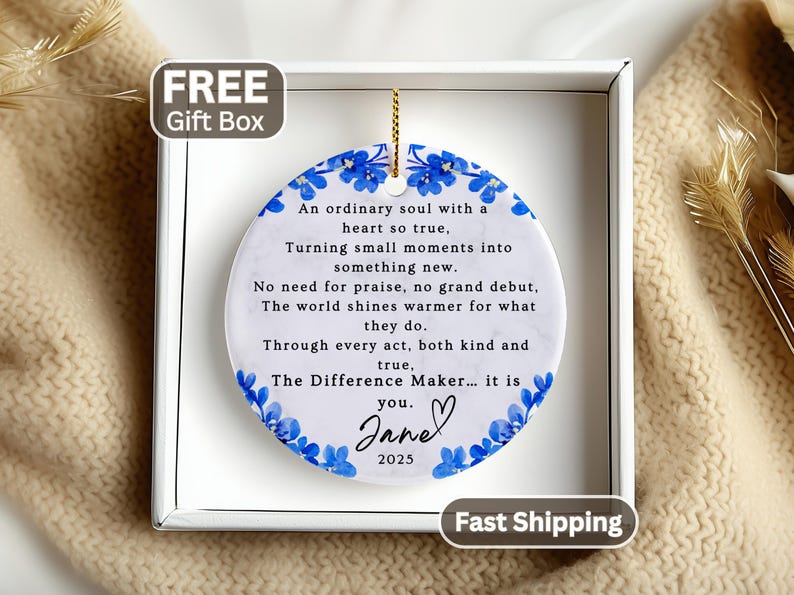 May include: A round white ceramic ornament with a marble texture, featuring a blue floral border and black printed text that reads: An ordinary soul with a heart so true, Turning small moments into something new. No need for praise, no grand debut, The world shines warmer for what they do. Through every act, both kind and true, The Difference Maker... it is you. Jane 2025.