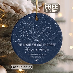 May include: A navy blue ceramic ornament with a constellation design and the text "THE NIGHT WE GOT ENGAGED" with names and a date. A gold string is attached for hanging. Includes a "FREE Gift Box" label.
