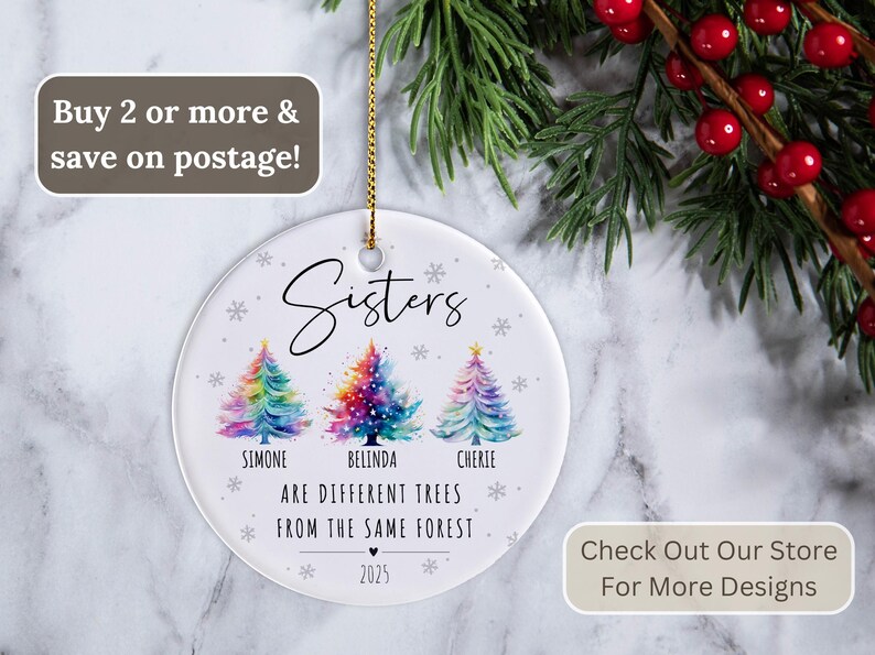 May include: A round white ceramic Christmas ornament featuring three watercolor-style Christmas trees in rainbow colors. The text reads: Sisters are different trees from the same forest, with the names Simone, Belinda, and Cherie, and the year 2025.