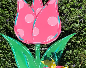 May include: A large, wooden tulip decoration with a pink polka-dotted flower head and green leaves. The flower has a turquoise outline and a colorful ribbon bow. The text "Starr Events" is visible on the leaves.