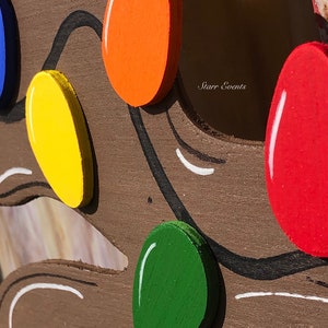 May include: Close-up of a wooden decoration featuring colorful, painted light bulbs in red, orange, yellow, green, and blue. The bulbs are attached to a brown wooden base with black and white painted accents. The text "Starr Events" is visible.