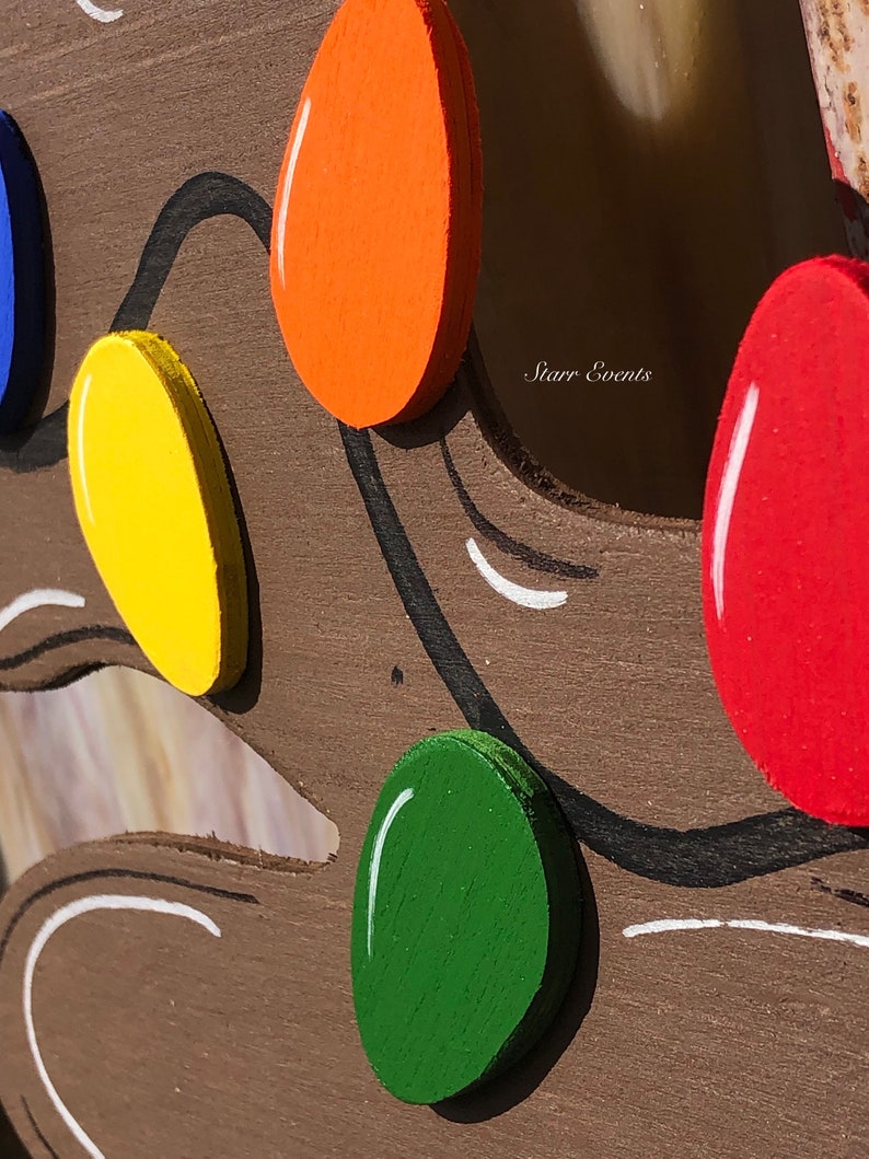 May include: Close-up of a wooden decoration featuring colorful, painted light bulbs in red, orange, yellow, green, and blue. The bulbs are attached to a brown wooden base with black and white painted accents. The text "Starr Events" is visible.