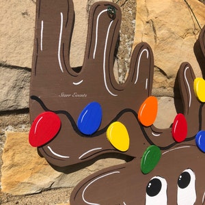 May include: A wooden reindeer Christmas decoration with brown antlers and a smiling face. The antlers are decorated with colorful lights in red, blue, yellow, orange, and green. The reindeer has a red glitter nose.