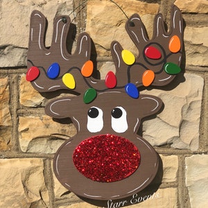 May include: A wooden reindeer Christmas decoration with a brown body, white accents, and a red glitter nose. The antlers are adorned with colorful Christmas lights. The text "Starr Events" is written on the bottom.