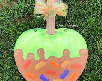 May include: A wooden apple-shaped decoration with a green top and brown base, resembling a caramel apple. It features colorful sprinkles and a decorative bow. The text "Starr Events" is visible.