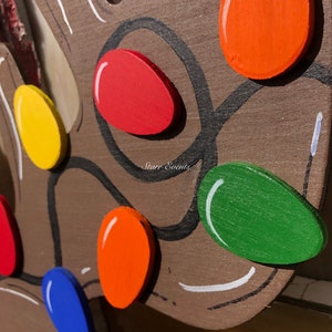 May include: Close-up of a wooden reindeer head with colorful, painted Christmas lights. The lights are in various colors, including red, orange, yellow, green, and blue. The reindeer is brown with black outlines and white accents.