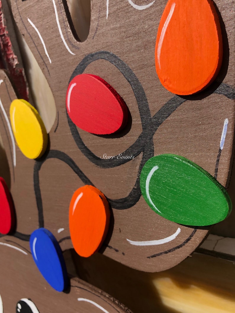 May include: Close-up of a wooden reindeer head with colorful, painted Christmas lights. The lights are in various colors, including red, orange, yellow, green, and blue. The reindeer is brown with black outlines and white accents.