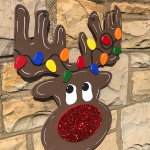 May include: A wooden reindeer Christmas decoration with a brown body, white accents, and colorful lights on the antlers. The reindeer has a red glitter nose and the text "Starr Events" in the upper left corner.