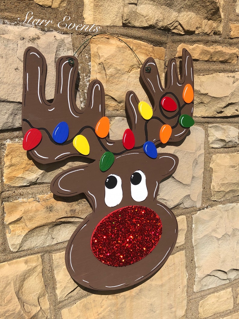 May include: A wooden reindeer Christmas decoration with a brown body, white accents, and colorful lights on the antlers. The reindeer has a red glitter nose and the text "Starr Events" in the upper left corner.