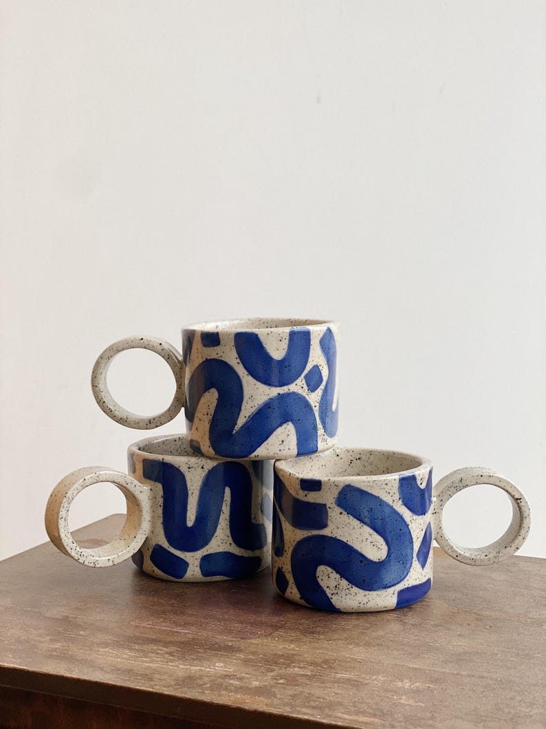 May include: Three ceramic mugs with blue and white abstract designs and large, round handles.