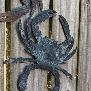 May include: Two metal crab sculptures attached to a wooden fence. The crabs are painted a dark blue-grey color.