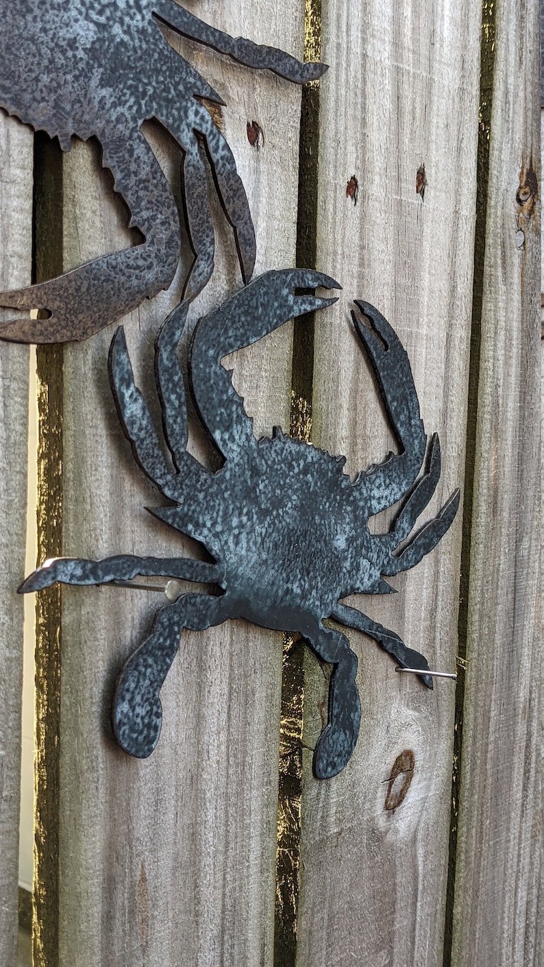May include: Two metal crab sculptures attached to a wooden fence. The crabs are painted a dark blue-grey color.